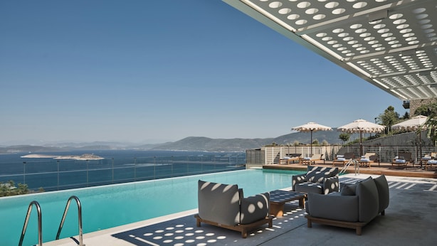 A poolside area with lounge chairs and umbrellas, overlooking a clear blue sea and distant mountains. - WAM by Karma (Bodrum)