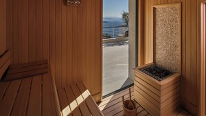 A sauna room with wooden walls, a bench, a stone wall, and a view of the sea. - WAM by Karma (Bodrum)