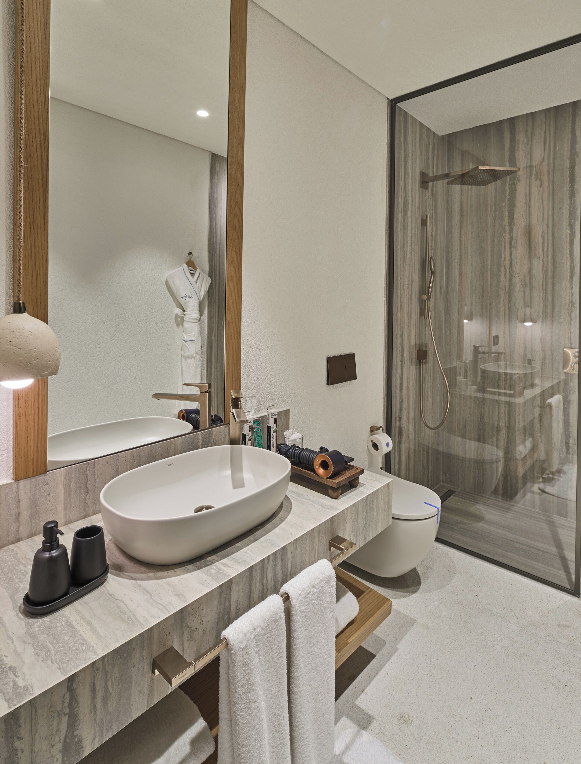 Un baño moderno con un lavabo ovalado grande, un inodoro, cabina de ducha con mampara de vidrio y un espejo amplio.