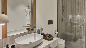 Un baño moderno con un lavabo ovalado grande, un inodoro, cabina de ducha con mampara de vidrio y un espejo amplio.
