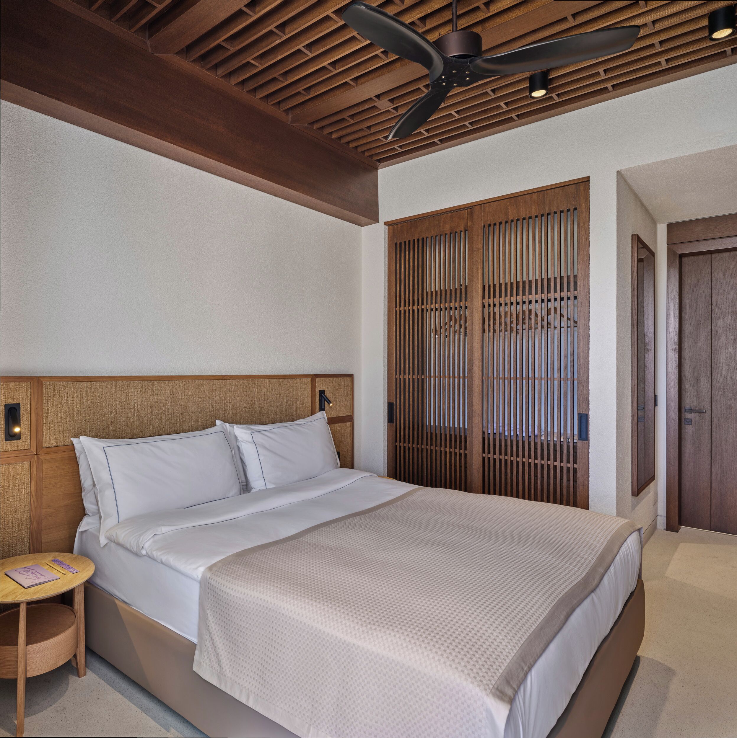 A bedroom with a wooden headboard, a bed with white bedding, a ceiling fan, and a wooden wardrobe.