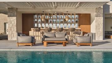 A poolside area with outdoor seating, a bar with bottles, and a stone wall.