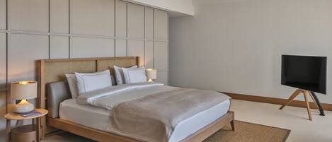 A neatly arranged bedroom with a bed, bedside lamps, a flat-screen TV, and a woven rug.