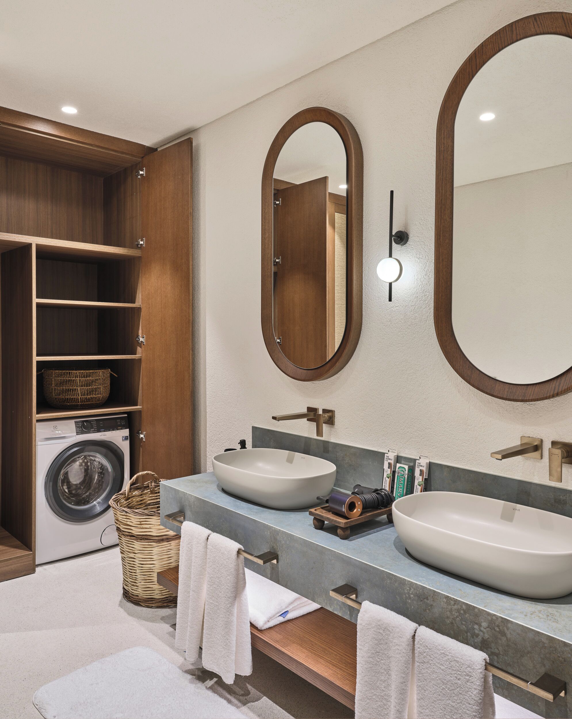 A modern bathroom with a double sink, a washing machine, and a large mirror.
