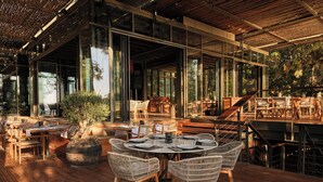 An outdoor dining area with wicker furniture, large windows, and a wooden deck. - WAM by Karma (Bodrum)
