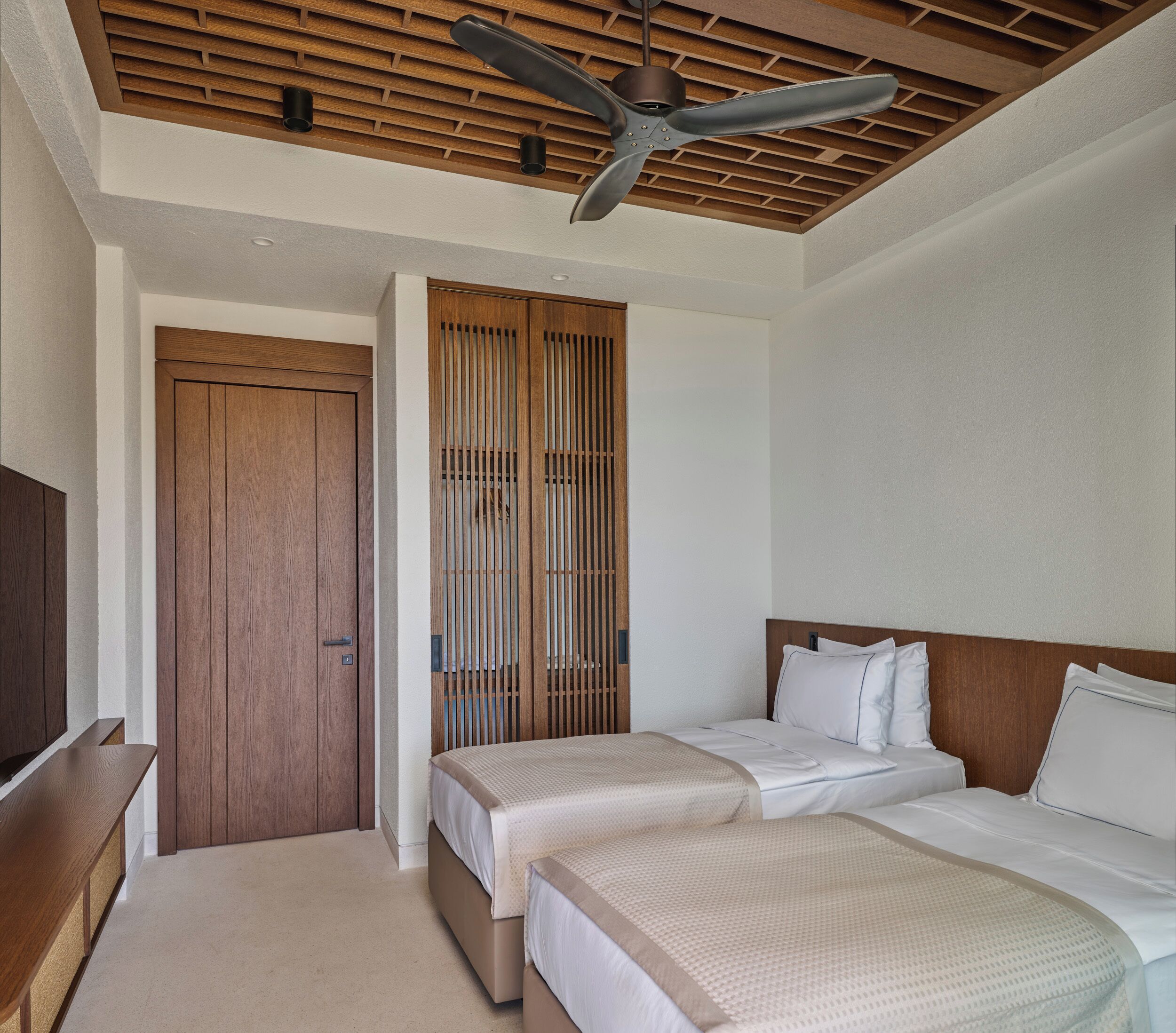 Une chambre d’hôtel avec deux lits, un ventilateur de plafond, une porte en bois et une armoire.