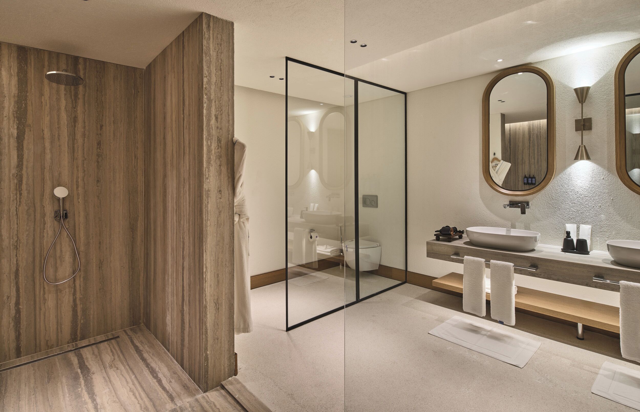 Un bagno moderno con cabina doccia in legno, parete divisoria in vetro, specchio grande e lavabo bianco con bacino a incasso.