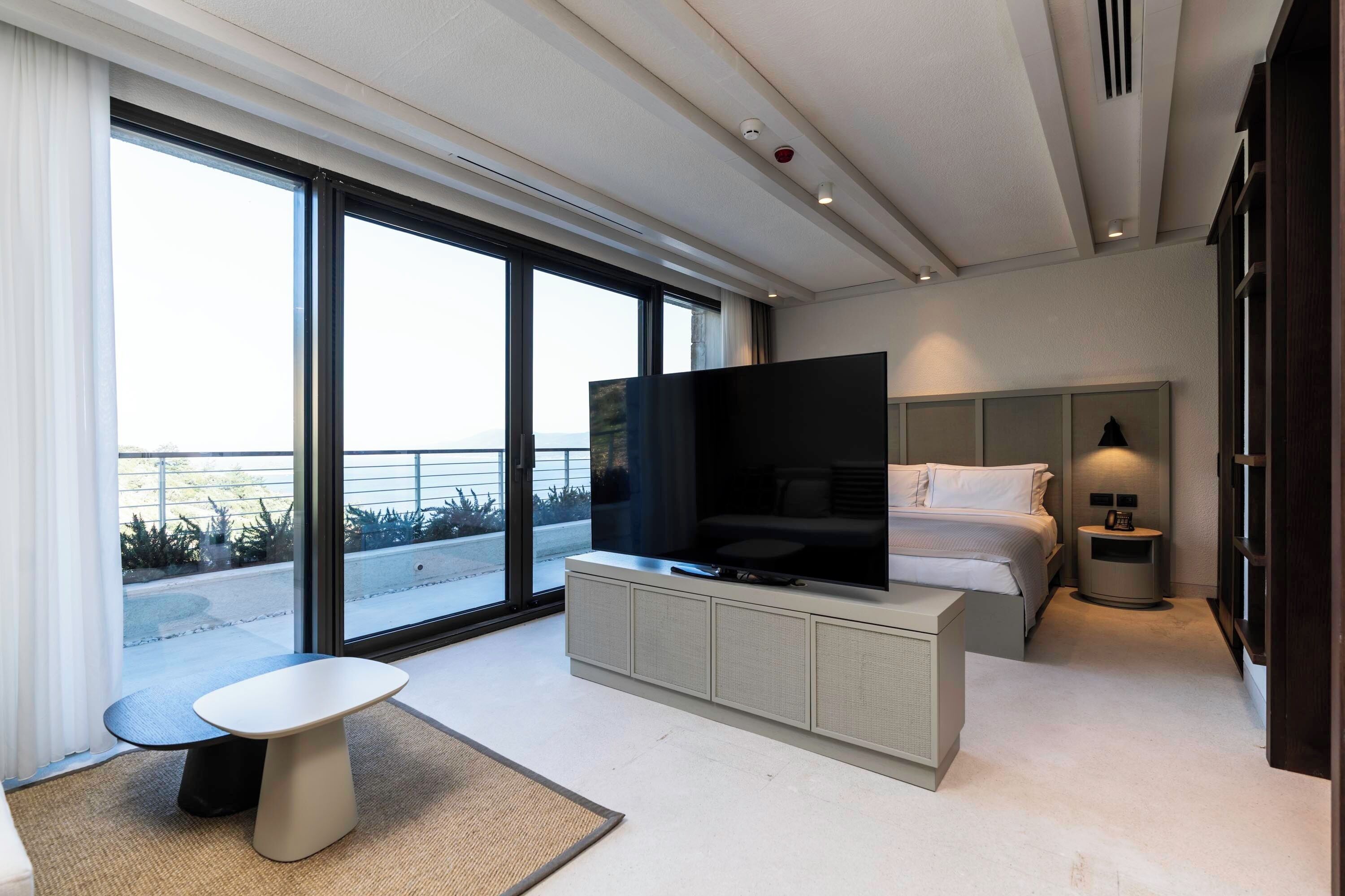 Ett modernt hotellrum med en stor TV, en säng, ett sängbord, ett litet bord och utsikt över omgivningarna.