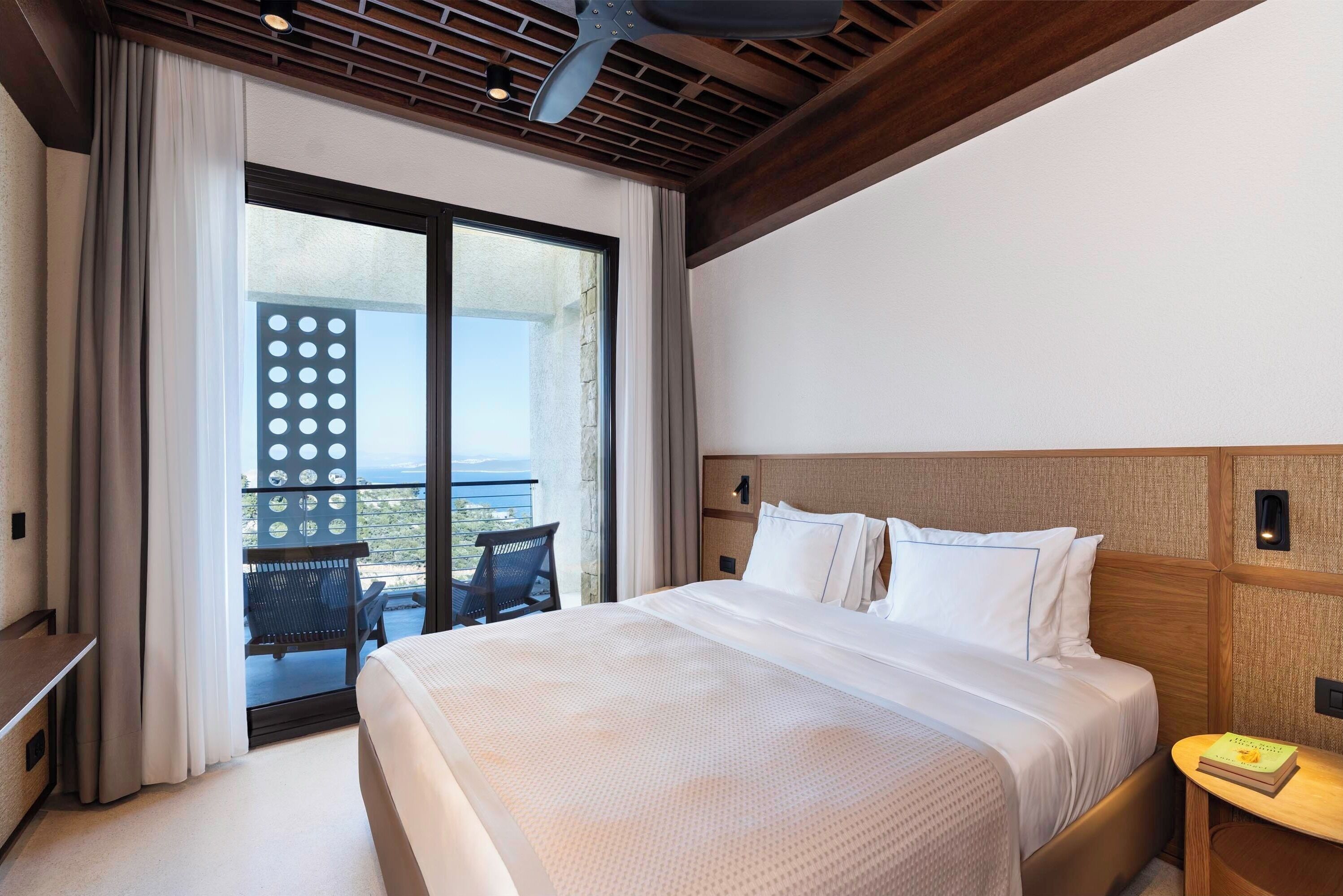 A hotel room with a large bed, a desk, a chair, and a balcony with a view.