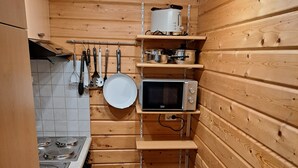 A compact kitchen with wooden walls, a stove, a microwave, and hanging utensils.