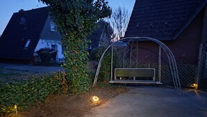 A paved pathway leading to a swing set in a residential area with houses in the background.