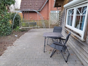 A patio with a table and chairs, a garden structure, and a wooden fence.