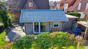 A small wooden house with a blue tiled roof, a front porch, and a garden area.