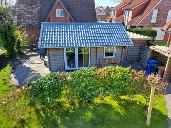 A small wooden house with a blue tiled roof, a front porch, and a garden area.