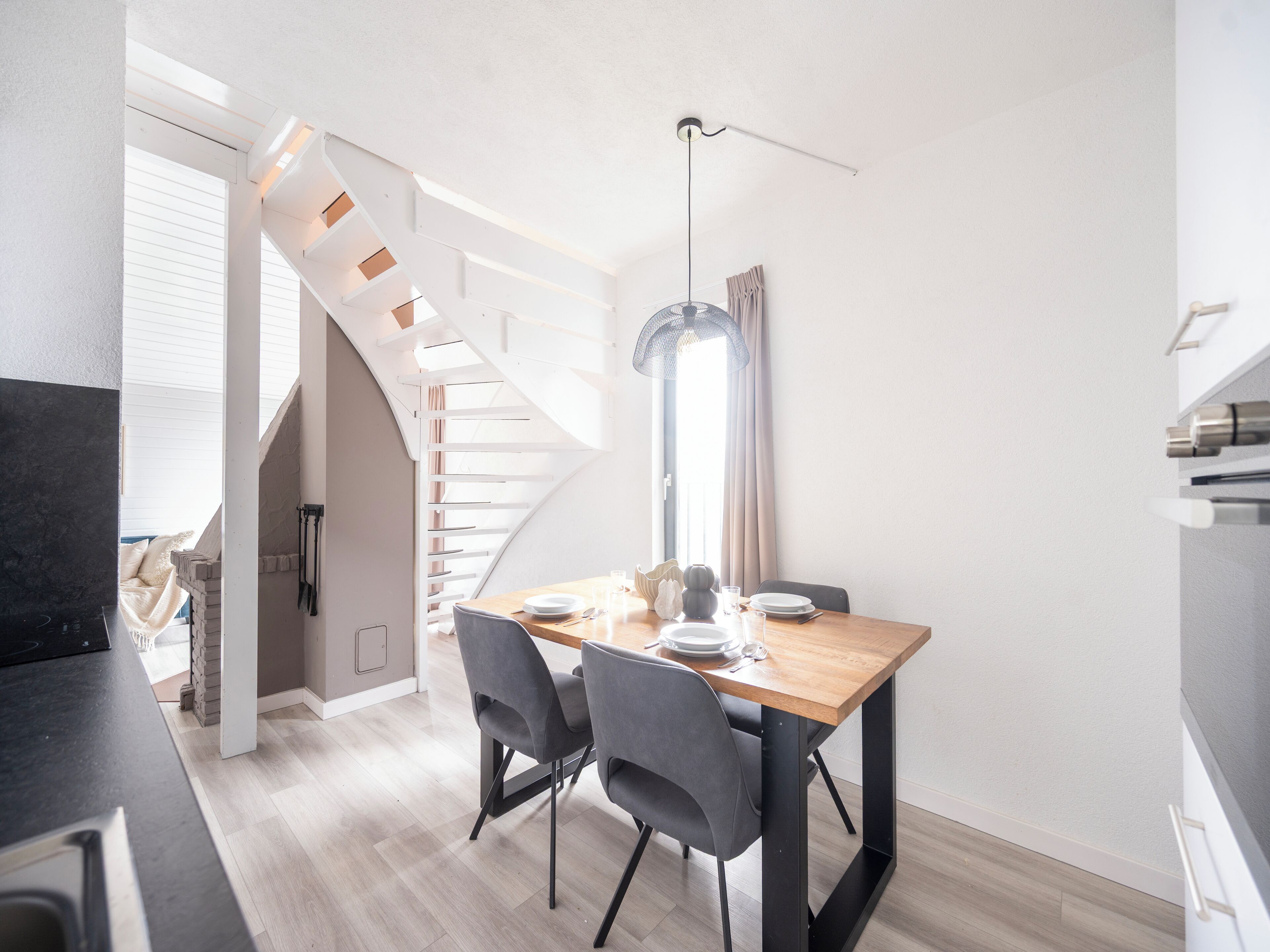 Una cucina moderna con un tavolo in legno, sedie grigie e una scala che conduce a un piano superiore.