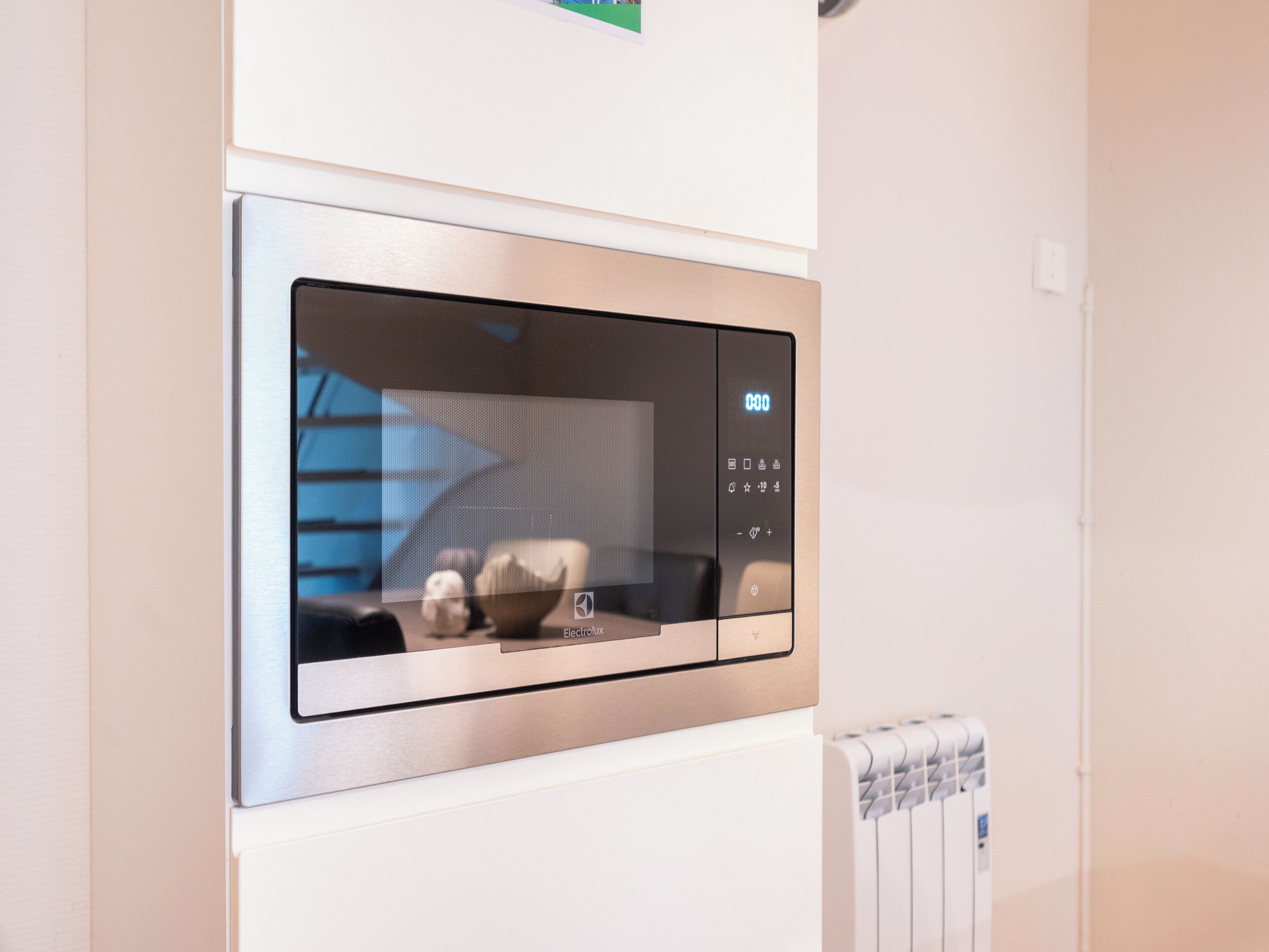 A modern kitchen with a built-in microwave, a digital clock, and a visible water dispenser.