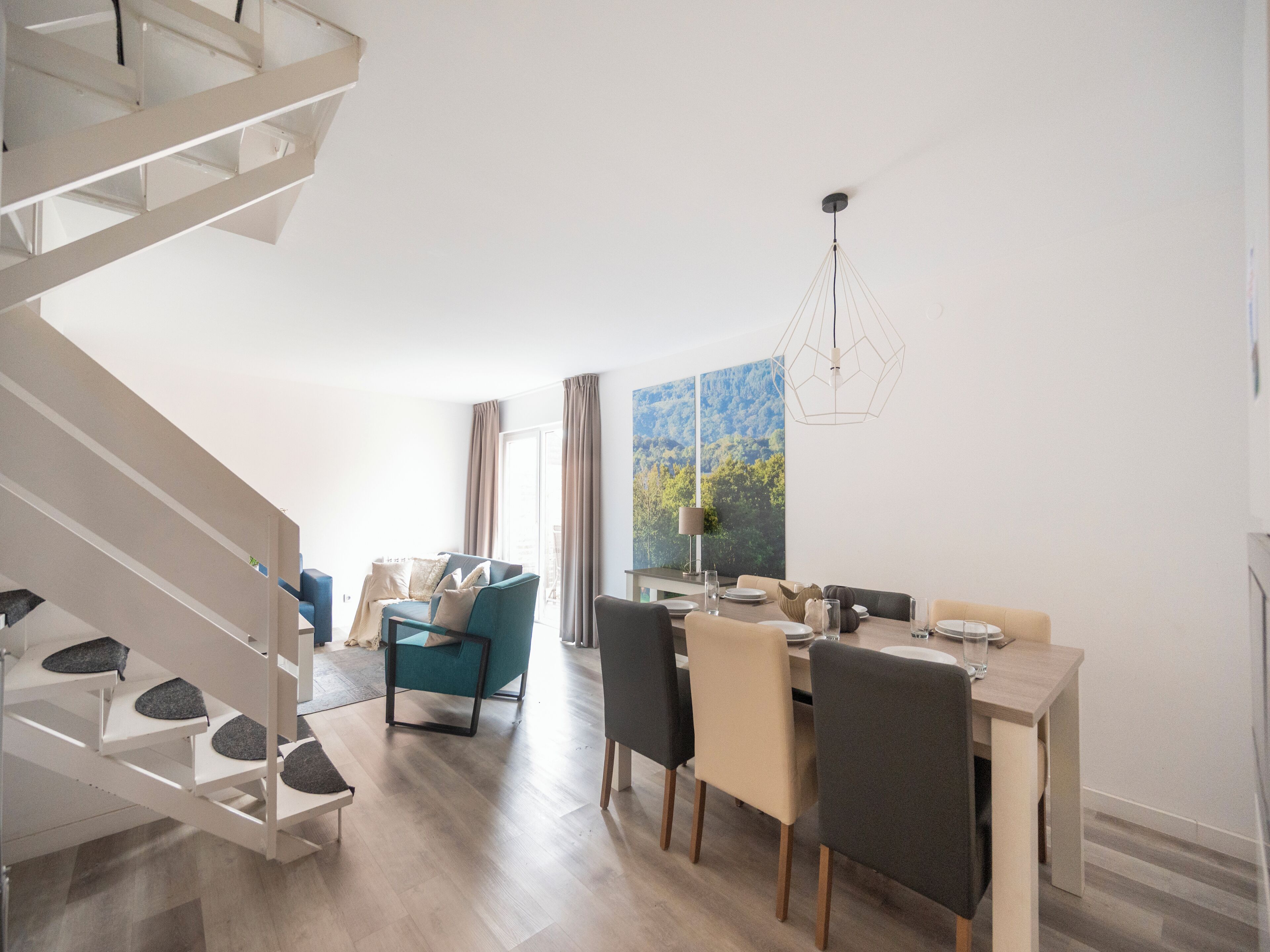 Un interior moderno con zona de comedor, escalera y un gran ventanal con cortinas.