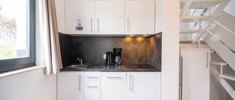 A compact kitchen with white cabinets, a black countertop, and a window with curtains.