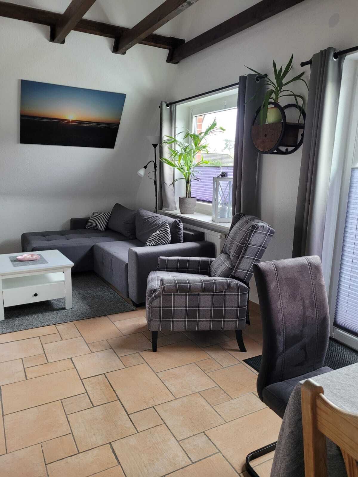 A modern living room with a sectional sofa, a plaid armchair, a small white table, and a large window with curtains.