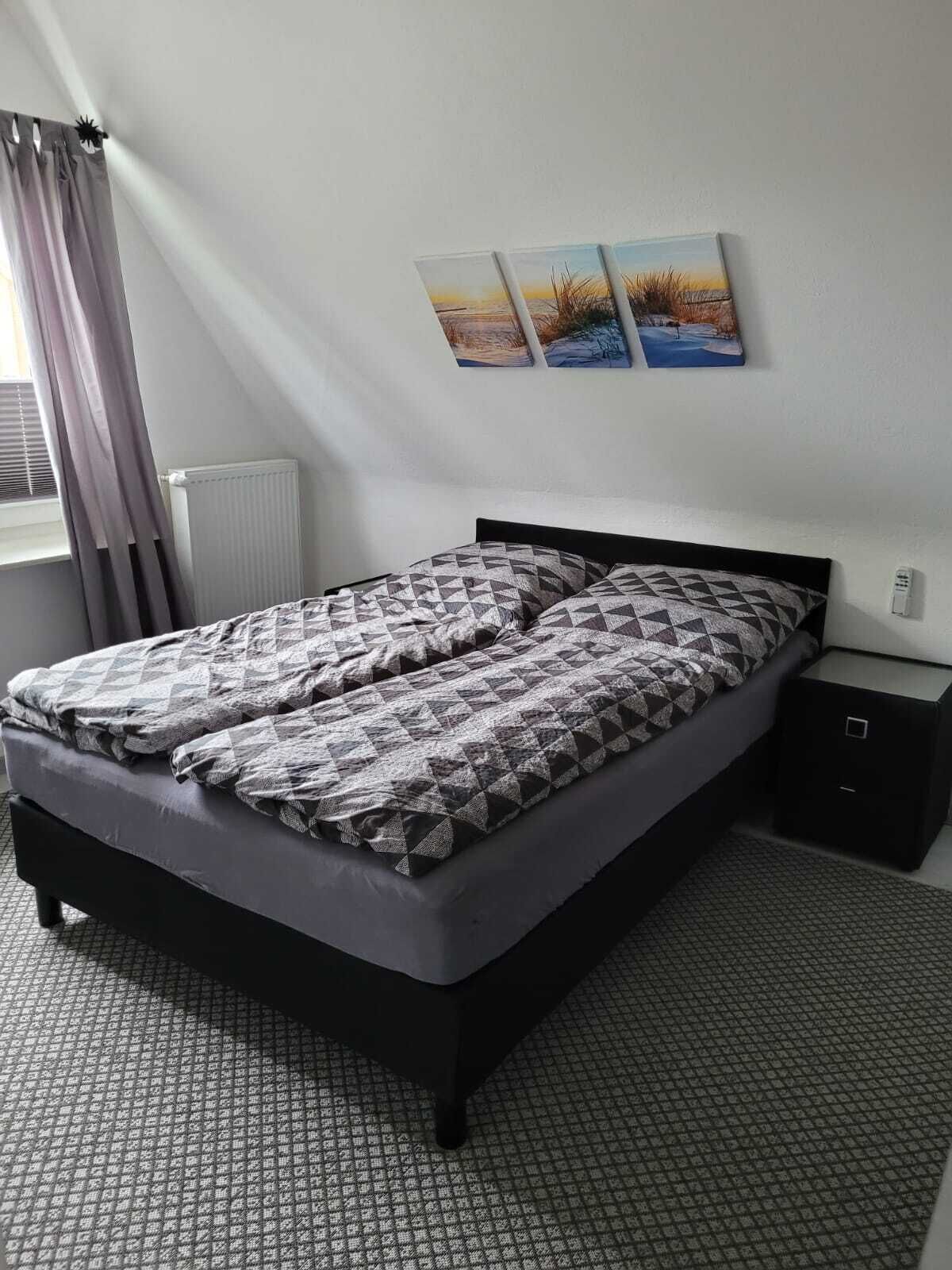 Un dormitorio con una cama, una mesita de noche, un radiador y una ventana con cortinas.