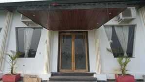 Un edificio con un alero de madera, una puerta de vidrio con diseño decorativo y macetas con plantas a ambos lados de la entrada.