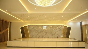 Un amplio vestíbulo con un mostrador de recepción de mármol, iluminación empotrada y un elemento decorativo en el techo.