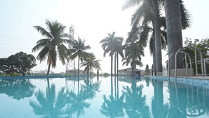 Una piscina cristalina con reflejos de palmeras y una estructura metálica al fondo.