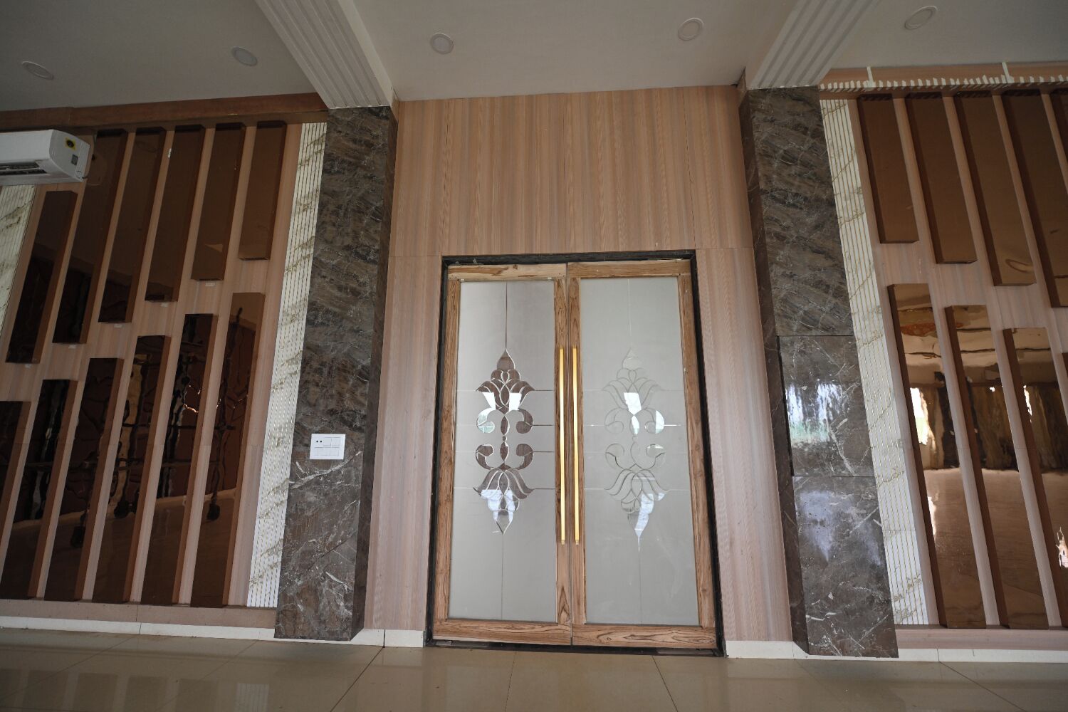 A hotel entrance with a wooden panel design, a glass door with a decorative pattern, and a stone accent wall.