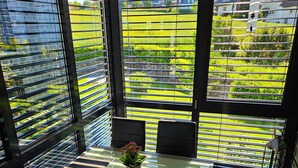 A modern dining area with a glass table, black chairs, and a view of a green landscape through large windows.