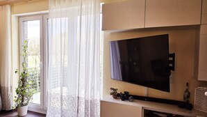 A living room with a large flat-screen TV, a potted plant, and a sliding glass door leading to a balcony.