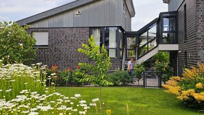 A modern building with a brick facade, a glass entrance, and a well-maintained garden with flowers.