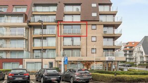 Un immeuble résidentiel à plusieurs étages, avec un panneau indiquant un parking, un panneau indiquant la direction de la côte ouest, et plusieurs voitures garées devant.