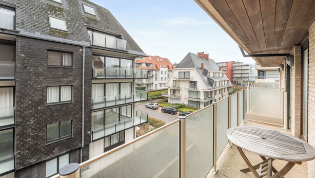 Un immeuble d’appartements moderne doté d’un balcon agrémenté d’une table et de chaises en bois.