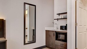 A modern kitchen with a large mirror, wooden cabinets, a countertop, and a microwave. - Studio6 Rock Springs, WY - Flaming Gorge (Rock Springs)