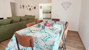 Een eethoek met een tafel gedekt voor vier personen, omringd door stoelen, een groene bank en een keuken op de achtergrond.