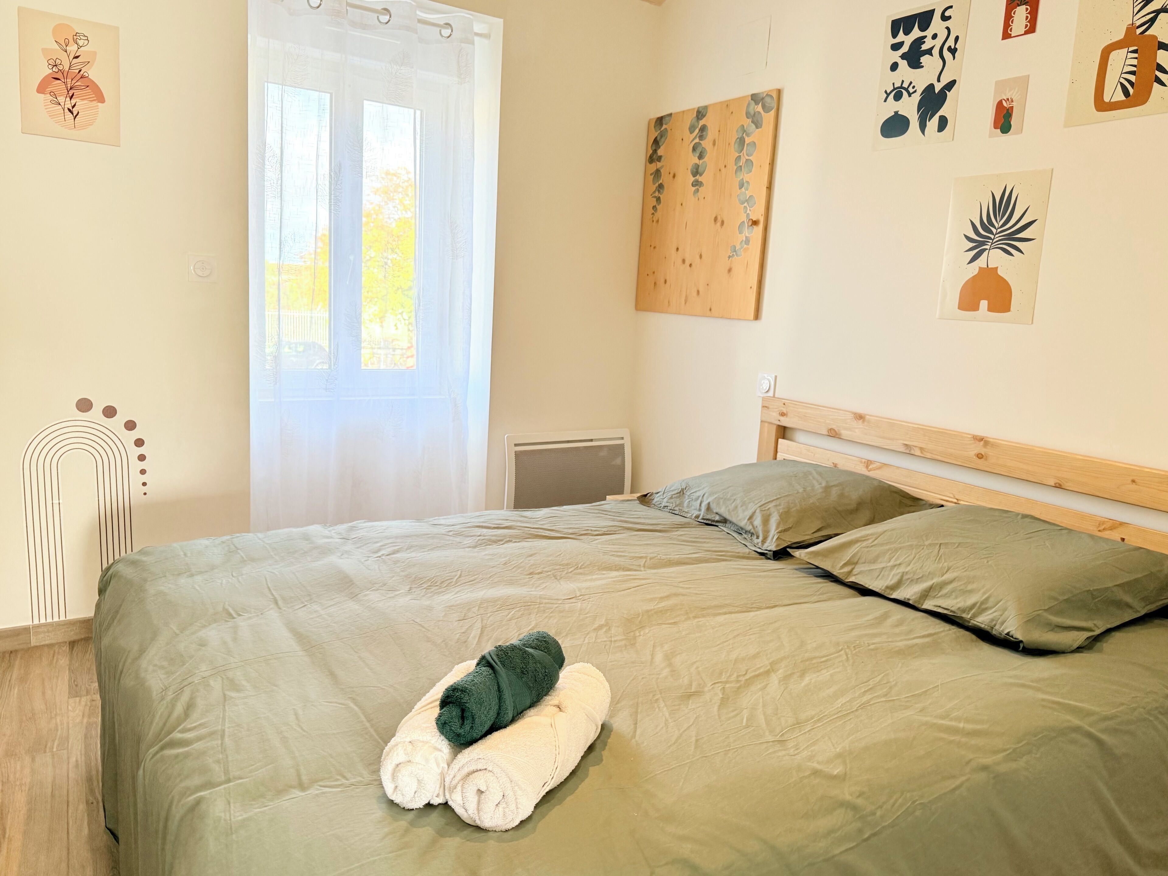 A neatly made bed with a green and white bedspread, two pillows, and a rolled towel on the bed.