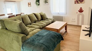 Een woonkamer met een groene bank, een houten bijzettafeltje en een televisie op een standaard.
