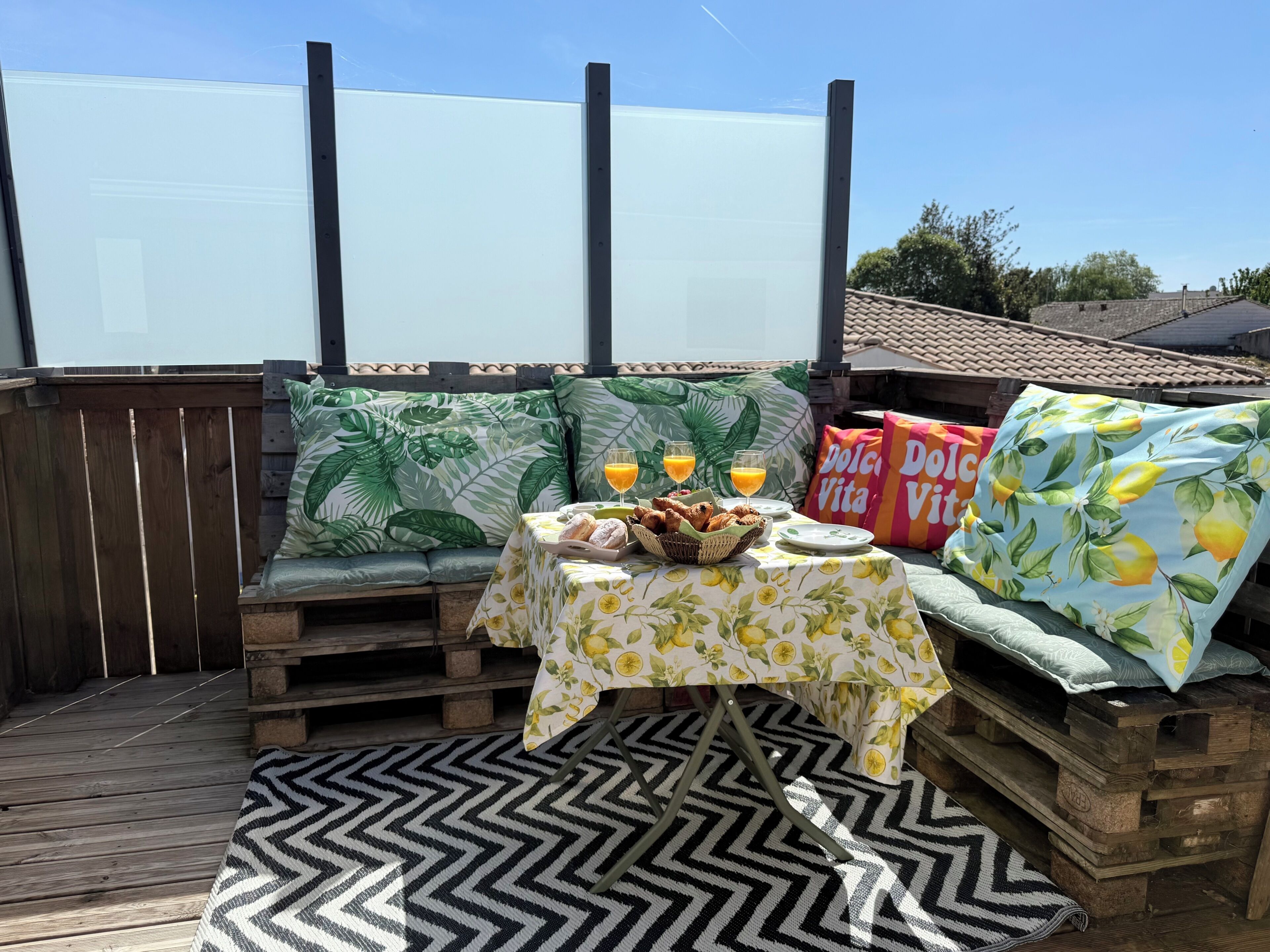 Een houten terras met een ontbijttafel, een met kussens beklede bank en uitzicht op de lucht.