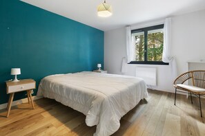 A bedroom with a bed, a nightstand, a chair, and a window with curtains. - Bright, Quiet 3-Bedroom Apartment with Wifi, Parking, Near the Beach (Pornichet)