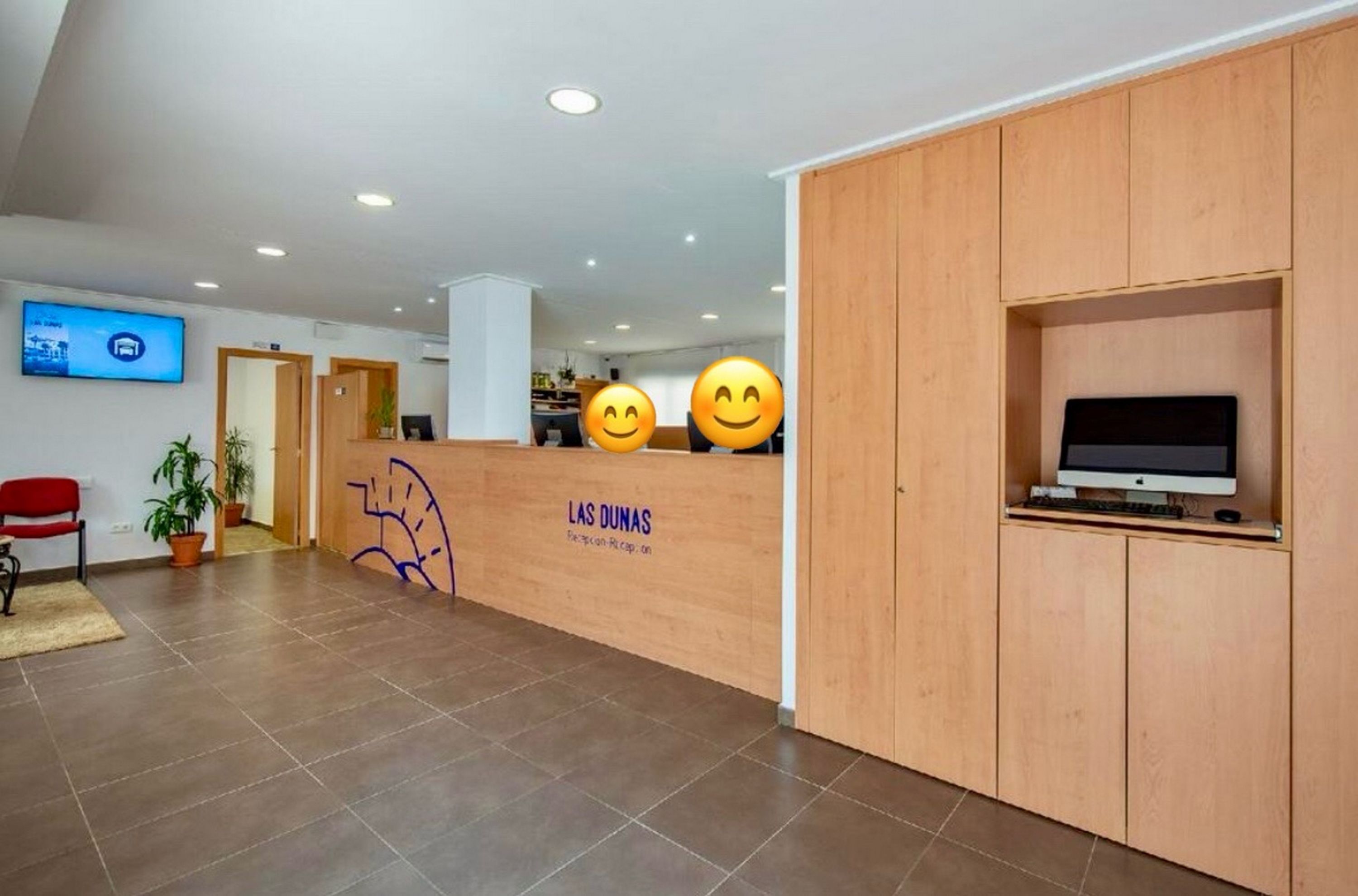 A reception area with a wooden desk, a computer, and a television on the wall.