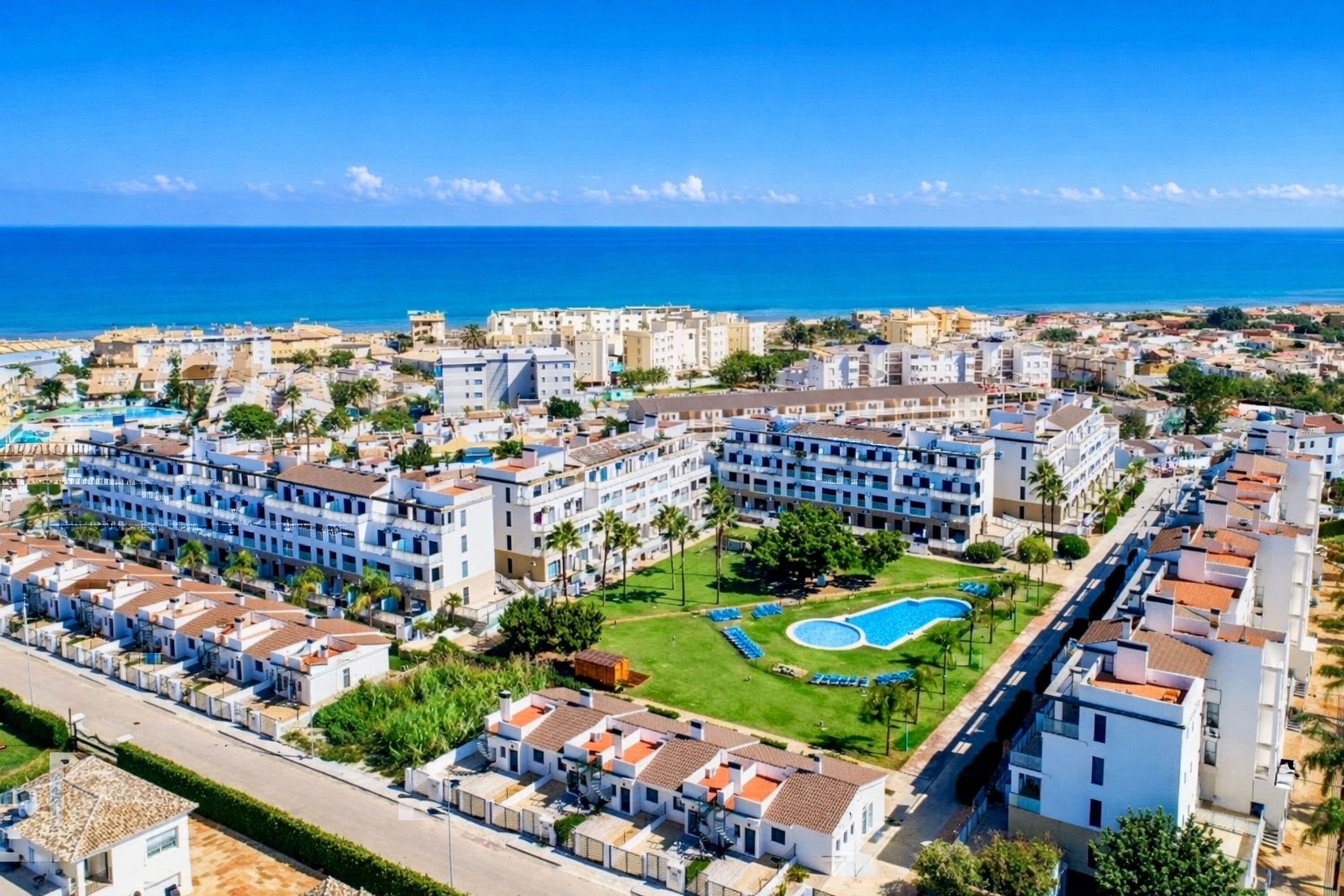 A coastal hotel with multiple buildings, a swimming pool, and a view of the sea.