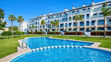 A modern hotel with a large swimming pool, multiple balconies, and lush landscaping.