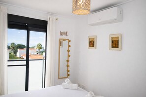 A hotel room with a large window, a bed, a vanity with a mirror, and a wall-mounted air conditioner. - Ap224 in Oliva With 2 Bedrooms and 1 Bathrooms (Oliva)