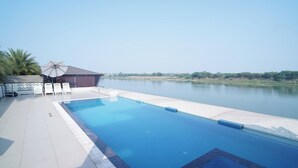 A swimming pool with a view of a lake, surrounded by a tiled deck and lounge chairs. - Riviera Resort and Hotels (Durg)