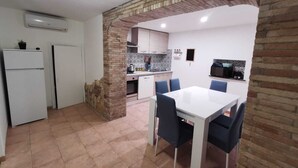 Uma cozinha compacta com área de jantar, apresentando um arco de tijolos, armários brancos e piso ladrilhado.