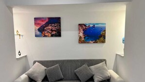 Uma sala de estar moderna com um sofá cinzento e duas pinturas emolduradas de paisagens na parede.
