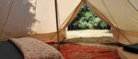Una tienda de campaña con una cama, un tapete rojo estampado y vistas al verdor exterior.