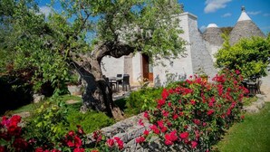 A rustic stone building with a white facade, a wooden door, and a small porch with outdoor seating. - Trulli Arco Antico (Locorotondo)