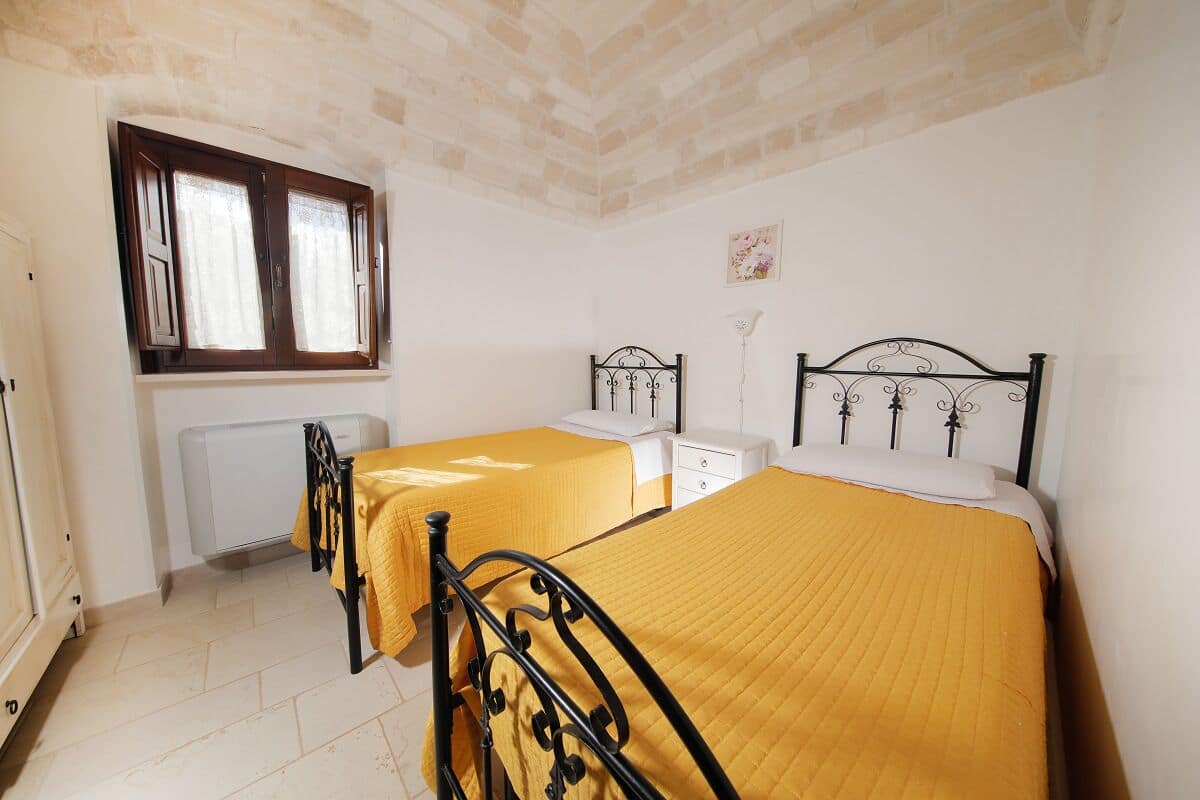Une chambre avec deux lits, un radiateur, une fenêtre et un mur blanc orné d’un tableau.