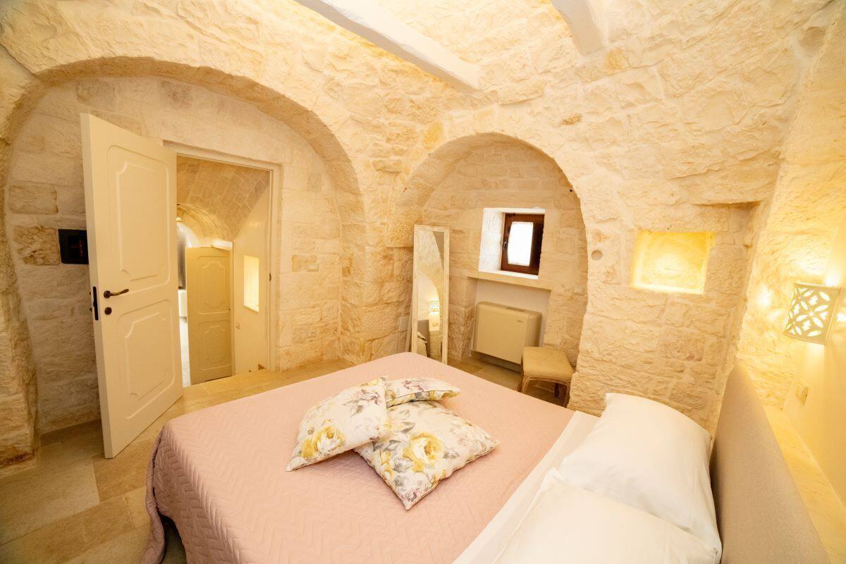 Une chambre avec un mur en pierre, un lit recouvert d’une literie à motifs floraux et une petite fenêtre.